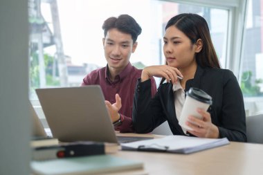 Genç iş arkadaşları dizüstü bilgisayara bakıyor ve ofiste mali verileri tartışıyorlar.