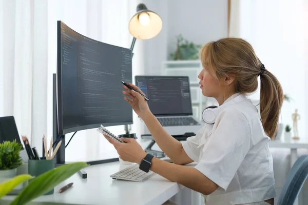 Young woman software developer working with program code on wide displays at modern office.