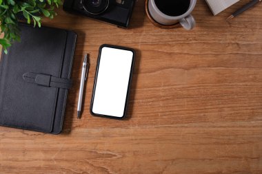 Beyaz ekranlı cep telefonu, kahve fincanı ve ahşap masadaki defter. Üst Manzara. Düz yatıyordu.