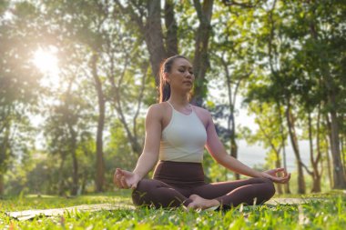 Calm millennial woman meditating and sitting in lotus pose on green grass. Concept of calm and meditation.	