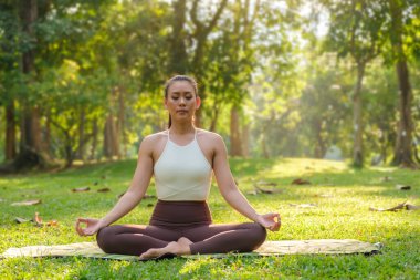 Peaceful millennial woman meditating with eyes closed at outdoor surrounded by beautiful nature.	