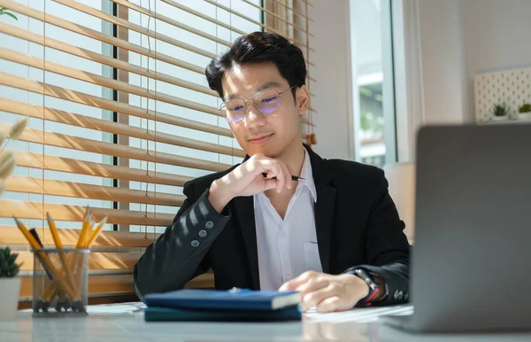 英俊的亚洲男性投资者在明亮的办公室里使用笔记本电脑处理文档 — 图库照片