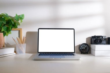 Dizüstü bilgisayarı, kamerası, kitapları ve beyaz masasında saksı bitkisi olan yaratıcı bir iş yeri. Reklam tasarımınız için boş ekran.