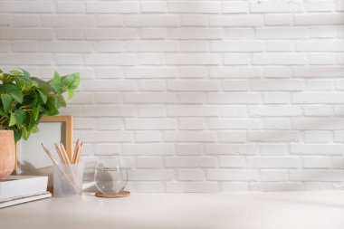 Kitaplar, kalem tutacağı, kahve fincanı ve tuğla duvara dayalı beyaz masa bitkisi olan ofis masası. Boşluğu kopyala.