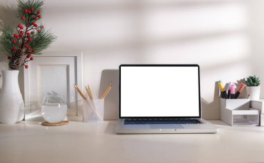 Boş ekranlı dizüstü bilgisayarın ön görüntüsü, beyaz masadaki resim çerçevesi ve kırtasiye malzemesi.