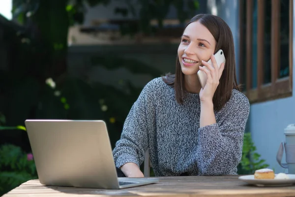 Χαμογελώντας Νεαρή Γυναίκα Χρησιμοποιώντας Φορητό Υπολογιστή Και Μιλώντας Στο Κινητό — Φωτογραφία Αρχείου