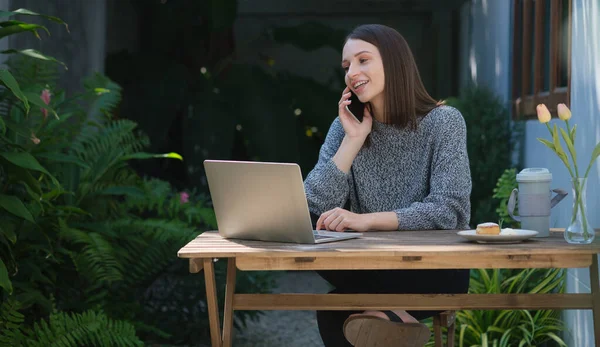Mujer Joven Sonriente Usando Ordenador Portátil Hablando Teléfono Móvil Mientras —  Fotos de Stock