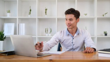 Modern iş yerinde dizüstü bilgisayar kullanan gülümseyen Asyalı iş adamı.