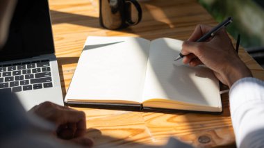 Dizüstü bilgisayar kullanan işadamlarının görüntüsünü kapat ve güneş ışığıyla not defterine not al..