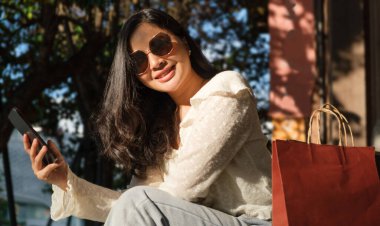 Alışveriş merkezinin yanındaki merdivenlerde oturan, alışveriş çantalı, neşeli, şık bir kadın..