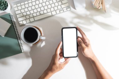 Beyaz ofis masasının üzerinde boş ekranı olan akıllı telefonu tutan adamın görüntüsünün üstünde..
