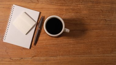 Kahve fincanının üst görüntüsü, yapışkan not defteri ve tahta masanın üzerindeki kalem. Metnin için boşluk kopyala.