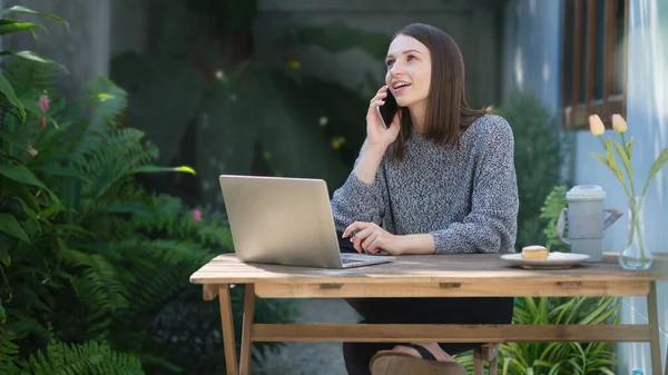 Mulher Bonita Usando Computador Portátil Falando Telefone Celular Enquanto Sentado — Fotografia de Stock