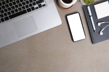 Akıllı telefon, dizüstü bilgisayar, not defteri ve kahve fincanı olan modern çalışma alanı gri masada..