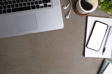 Laptop bilgisayarı, akıllı telefon, kahve fincanı ve gri masadaki not defteriyle modern çalışma alanı.