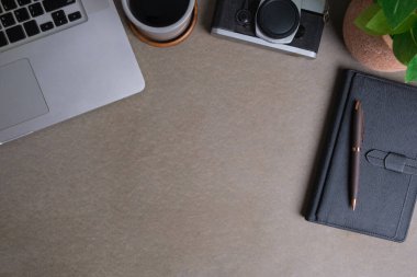 Gri arka planda dizüstü bilgisayarı, kamerası, defteri ve kahve fincanı olan şık bir iş yeri..