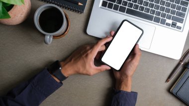 Modern çalışma alanının üstünde akıllı telefonları tutan adamın üst görüntüsü. Reklam tasarımınız için boş ekran.