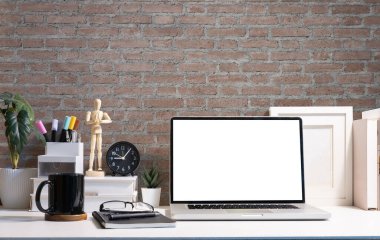 Laptop computer with empty display, coffee cup, picture frame and stationery on white table.	