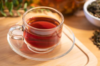 Arkaplanda kurutulmuş çay yaprakları ve tahtadan yapılmış taze demlenmiş siyah çay..