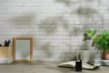 Home office desk with books, cup of coffee, stationery and potted plant on grey table.	