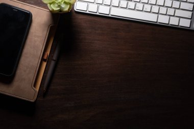 Akıllı telefon, defter, tahta masadaki kalem ve klavye. Metnin için kopyalama alanı olan üst görünüm.