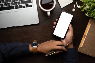 İşadamı elinde kalemle ahşap masada akıllı telefon kullanıyor..