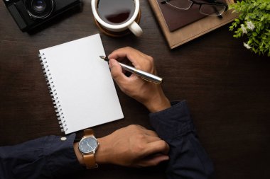 Businessman hand holding pen, writing on empty notepad. Above view, blank screen for your advertise design.	