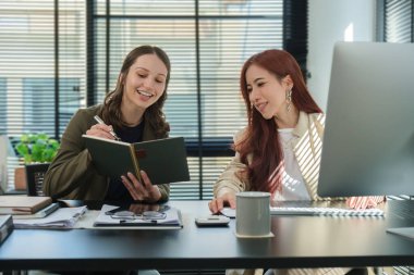 Two happy young female working on new creative project, using laptop in modern office.	