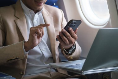 Uçak penceresinin yanında oturan ve akıllı telefon kullanan işadamının görüntüsü..