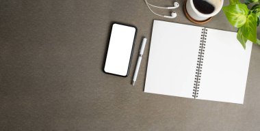 Boş defterli ofis masası, cep telefonu, kahve fincanı ve gri masadaki saksı bitkisi..