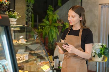 Kafkasyalı kadın girişimci, sıcak kahve dükkanının içinde tezgahın önünde dikilirken dijital tablet kullanıyor..