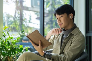 Mutlu Asyalı genç adam kablosuz kulaklık ve kafede kitap okumak, tatilde dinlenme zamanı..