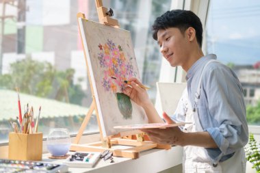 Creative man painting on canvas  in with oil paint in bright modern art studio. 