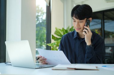 Handsome man financial advisor sitting at workplace and consulting customer on cellphone. 