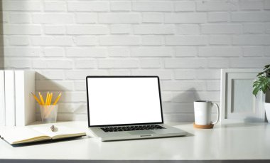 Mock up laptop computer with blank screen, coffee cup, picture frame and houseplant on white table.