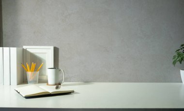 Contemporary workplace with picture frame, books and coffee cup on white table. Copy space for product display and presentation. 
