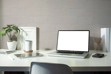 Laptop computer with blank display, tablet, coffee cup and houseplant on white table. Modern workplace.
