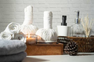 Beautiful spa composition on white table with, spa herbal compress balls, towels and burning candles. 
