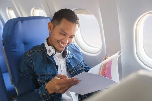 Young man in jean jacket reading   reading airliner magazine during flight.