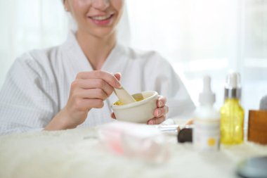 Cropped shot of young woman in bathrobe making homemade turmeric face mask in bowl. Facial spa treatment concept.