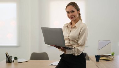 Successful businesswoman holding laptop and looking confidently to camera.