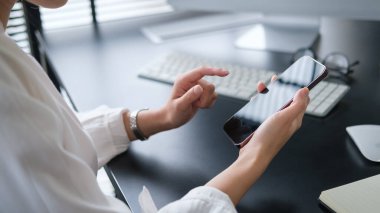 Smiling young woman using mobile phone on wooden office desk.	