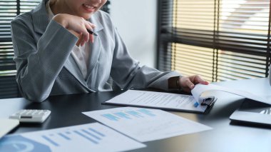 Gülümseyen Kafkas kadın yönetici modern ofiste otururken kağıt işi belgesi dolduruyor.