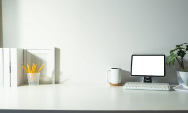 Digital tablet, books, picture frame and coffee cup on white table.