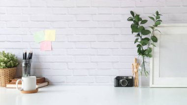 Creative workspace with retro camera, coffee cup, picture frame and houseplants on white table. Copy space for text.