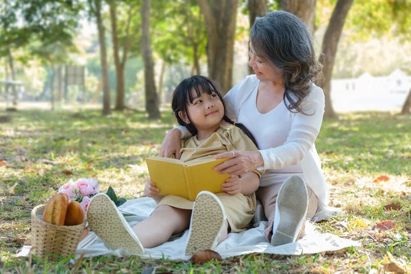 Loving mature grandmother telling story to her adorable granddaughter,  enjoy priceless time together at outdoor.