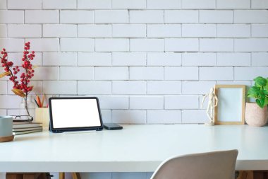 Comfortable workplace with digital tablet, picture frame, books and houseplant on white table.