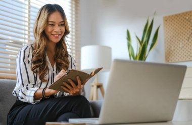 Etkileyici bir milenyum kadını dizüstü bilgisayarda internetten web sitesini izliyor ve deftere not alıyor..