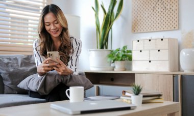 Woman hold with smart phone at sit on sofa and use phone happily at home.	