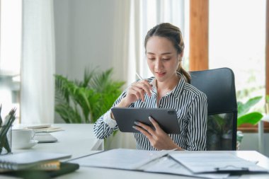 Smiling beautiful businesswoman holding stylus pen and writing information on digital tablet.	